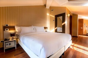 Ein Hotelzimmer mit einem großen Bett, einem Nachttisch mit Lampe, einem Safe und einem Spiegel.