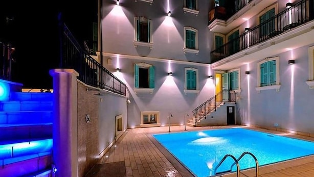 A swimming pool area with a wooden deck, a staircase, and a building with multiple balconies and windows. - Mefuta Hotel (Gardone Riviera)