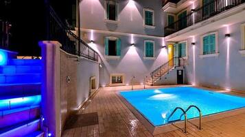 Zona piscina con solarium in legno, una scala e un edificio con numerosi balconi e finestre.