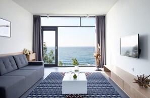 Sala de estar moderna com sofá, mesa de centro e uma grande janela com vista para o mar.