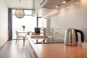 Cozinha moderna com chaleira de aço inoxidável, pia e área de refeições com cadeiras.