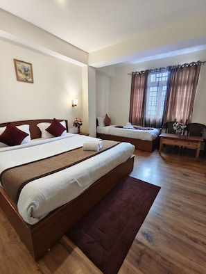 Une chambre d’hôtel avec deux lits, un plancher en bois, un tableau au mur et une fenêtre avec des rideaux.