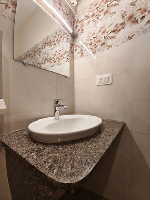 Une salle de bain dotée d’un comptoir en granit, d’un lavabo blanc, d’un robinet moderne et d’un miroir orné d’un papier peint à motifs floraux.