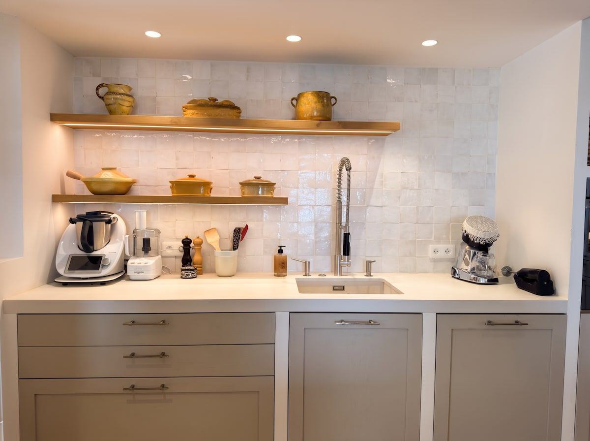 Een moderne keuken met witte kastjes, een spoelbak en een aanrecht met diverse keukenapparaten en keukengerei.