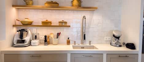 Een moderne keuken met witte kastjes, een spoelbak en een aanrecht met diverse keukenapparaten en keukengerei.