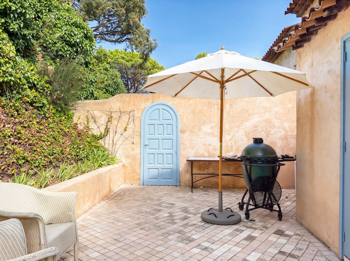 Une terrasse avec un barbecue, une table et un parasol.