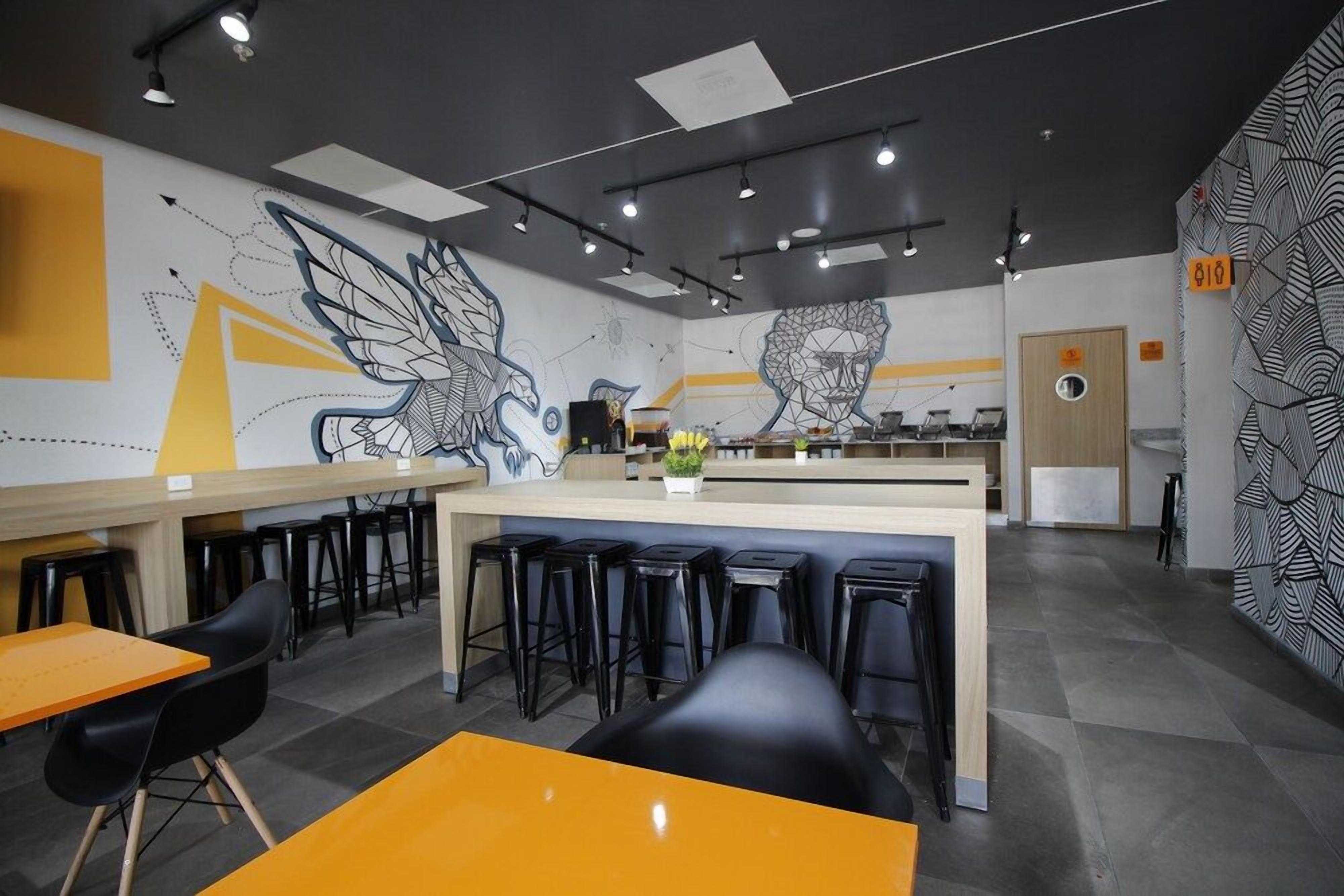 Interior moderno de una cafetería con barra central, taburetes negros y un mural en la pared.
