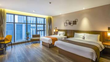 A hotel room with two beds, a desk, a chair, and a large window with curtains.