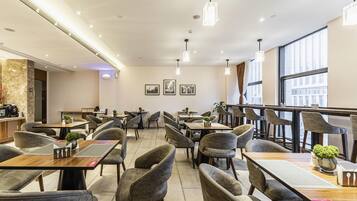 A modern restaurant interior with multiple dining tables and chairs, pendant lighting, and framed pictures on the walls.