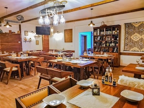 A restaurant with wooden tables and chairs, a wine rack, and a bookshelf filled with books and bottles. - Plivica Village Etno Garden (Plitvicka Jezera)