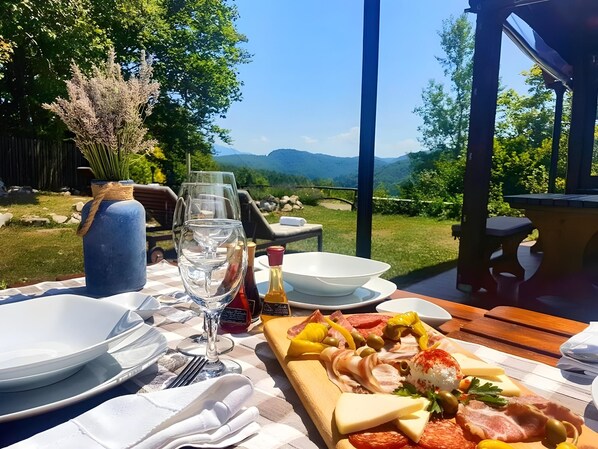 An outdoor dining area with a table set for a meal, a bottle of wine, and a view of the mountains. - Plivica Village Etno Garden (Plitvicka Jezera)