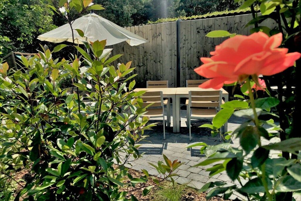Een terras met een tafel en stoelen, omringd door planten en een houten hek.