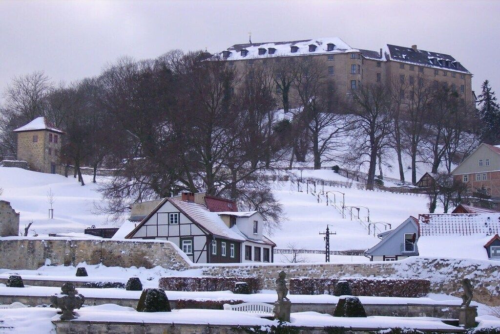 Un bâtiment historique doté d’une tour imposante, entouré d’arbres couverts de neige et d’une petite colline.