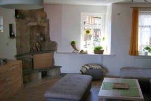 Ein gemütliches Wohnzimmer mit Kamin aus Stein, einem Fenster mit Aussicht, einem Tisch mit Schneidebrett und einer Couch.
