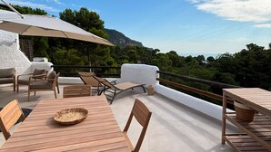 Een terras buiten met houten meubels, een tafel met een rieten mand en uitzicht op het landschap.