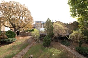 A courtyard with a large tree, a brick building, and a small garden area. - Soulful 1BDR Flat with Balconies in Kentish Town (Greater London)