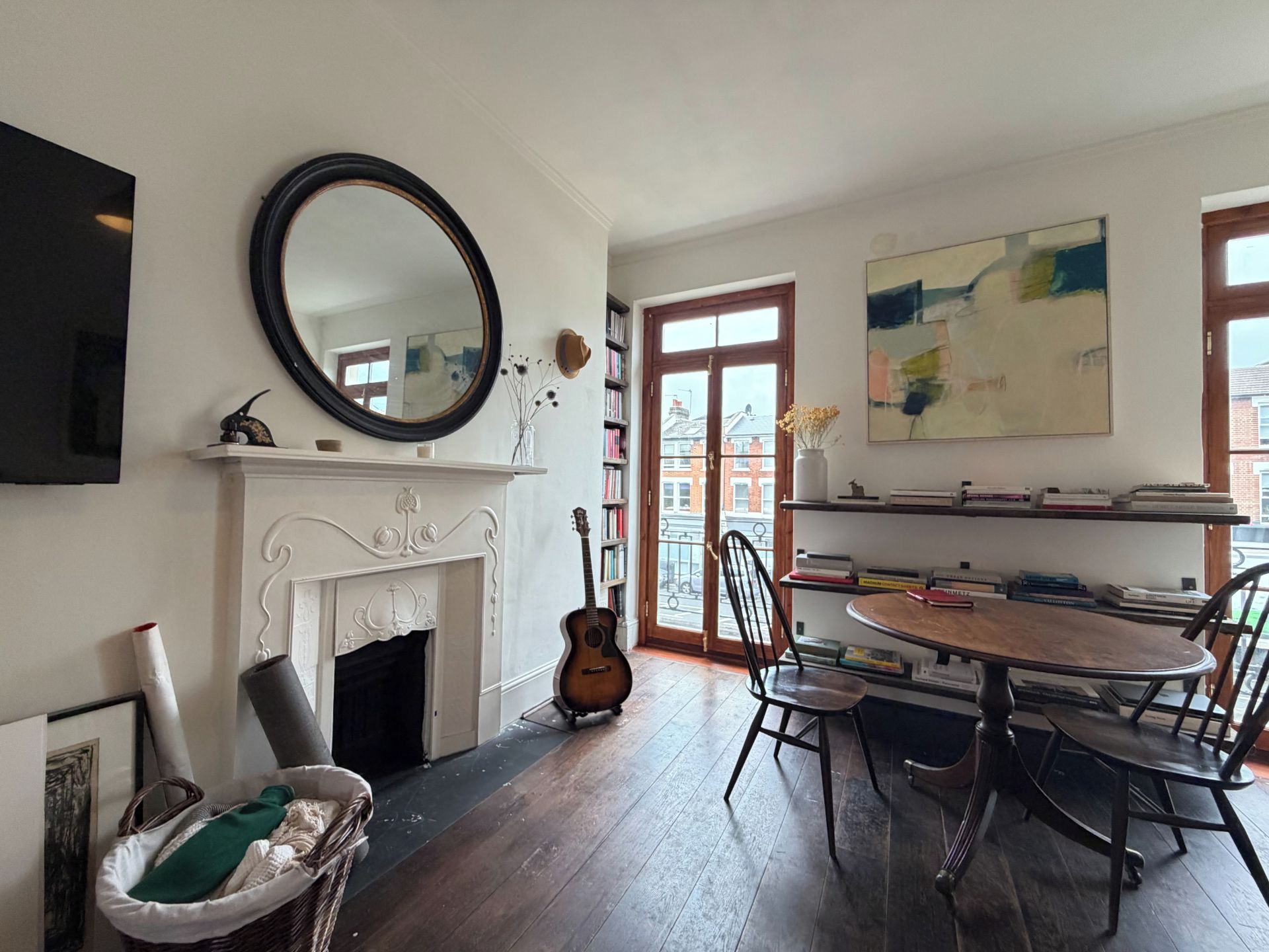 Une pièce avec une cheminée, une table à manger avec des chaises, une guitare, une bibliothèque et un grand tableau abstrait.