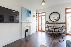 A dining area with a fireplace, a round mirror, and a view through a window. - Soulful 1BDR Flat with Balconies in Kentish Town (Greater London)