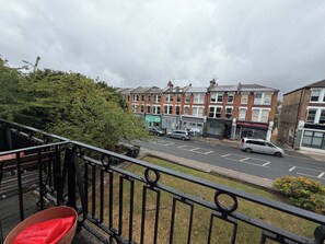 A balcony with a red chair, a view of a street with parked cars, and buildings with shops. - Soulful 1BDR Flat with Balconies in Kentish Town (Greater London)