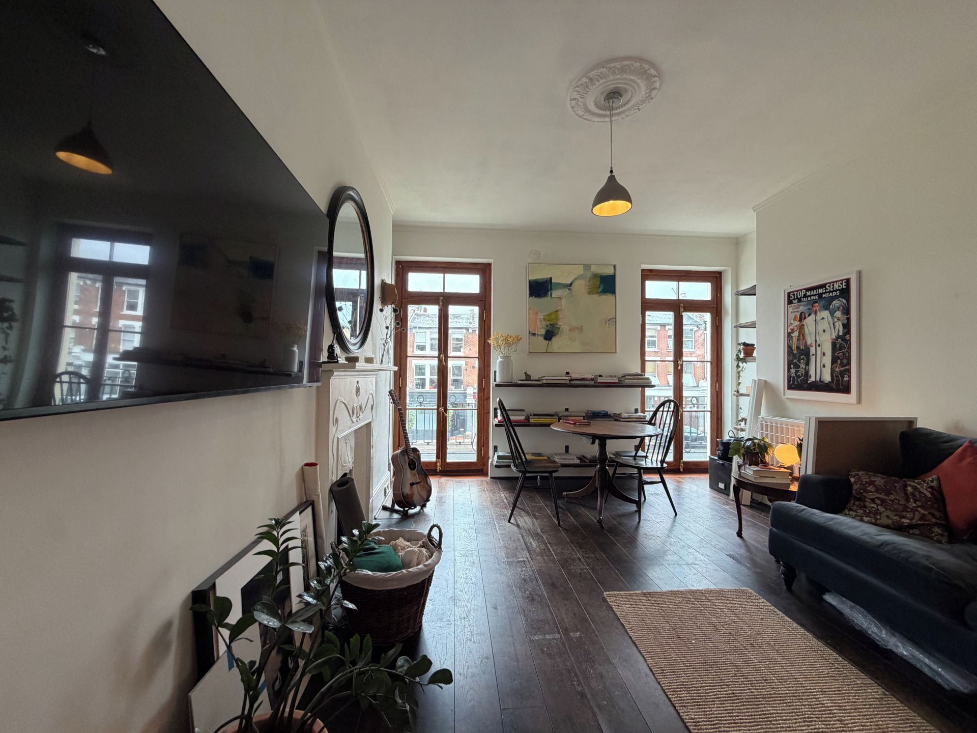 Ein geräumiges Wohnzimmer mit großem Fernseher, einer Essecke mit Holztisch und -stühlen sowie einer gemütlichen Sitzecke mit Sofa und Kissen.