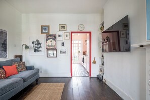 A living room with a grey sofa, a red door leading to a hallway, and various framed pictures on the walls. - Soulful 1BDR Flat with Balconies in Kentish Town (Greater London)