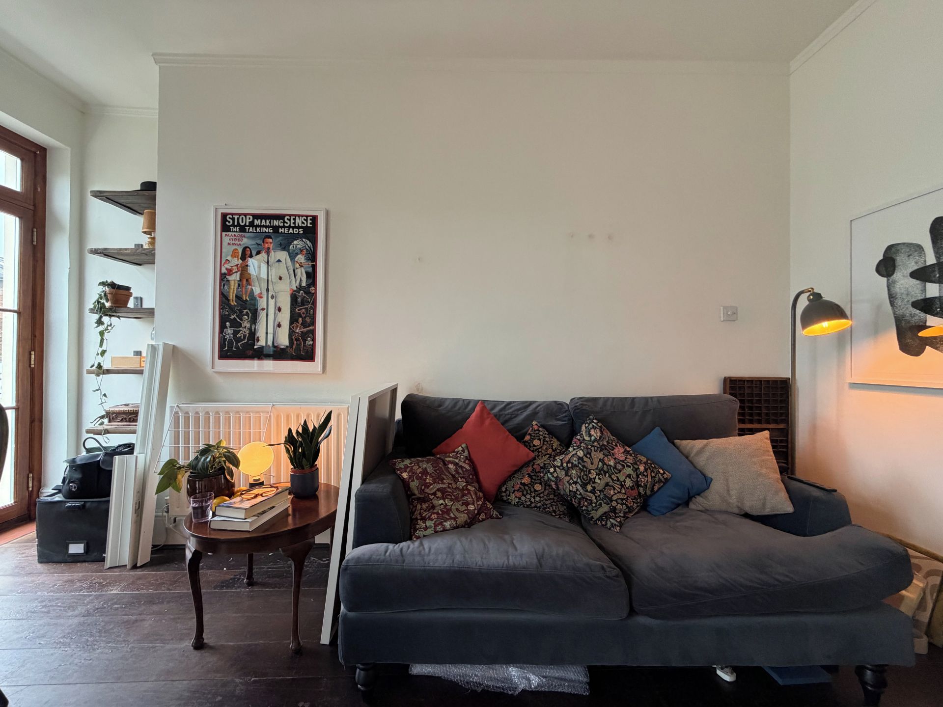 Un salon avec un canapé gris foncé, une petite table d’appoint en bois et une affiche accrochée au mur.
