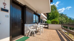 A hotel entrance with a dark wooden door, a small outdoor seating area with tables and chairs, and a view of a mountainous landscape. - Fiemmea – Hidden Chalet, Valley View in Cavalese (Cavalese)
