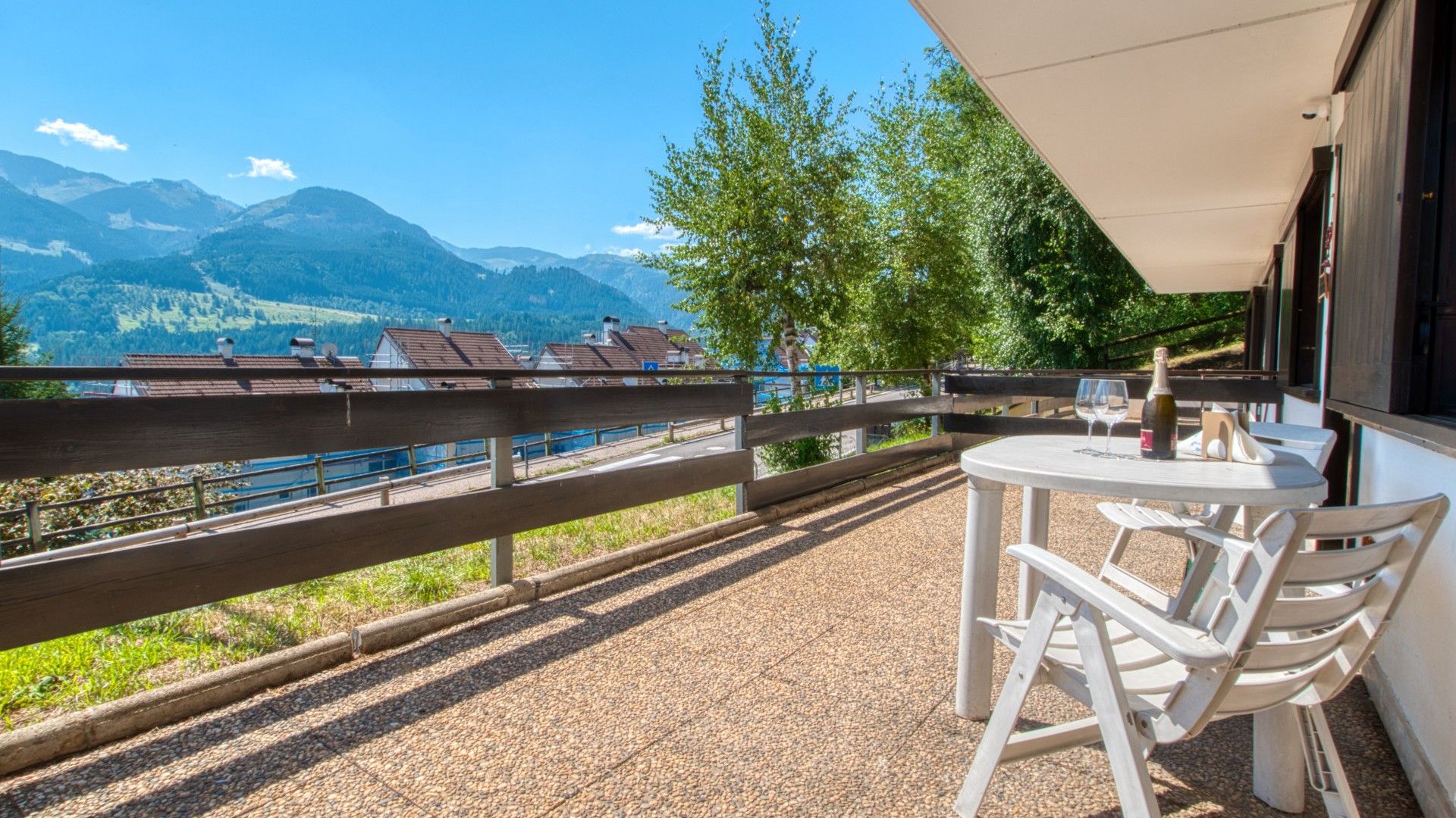 Eine Terrasse mit Bergblick, einem Tisch mit Stühlen und einer Weinflasche.