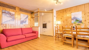 A cozy room with a red sofa, wooden dining table, chairs, and a kitchen area with cabinets and a TV. - Fiemmea – Hidden Chalet, Valley View in Cavalese (Cavalese)