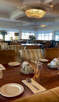 Un comedor con candelabro, mesas dispuestas con platos, vasos y cubiertos.