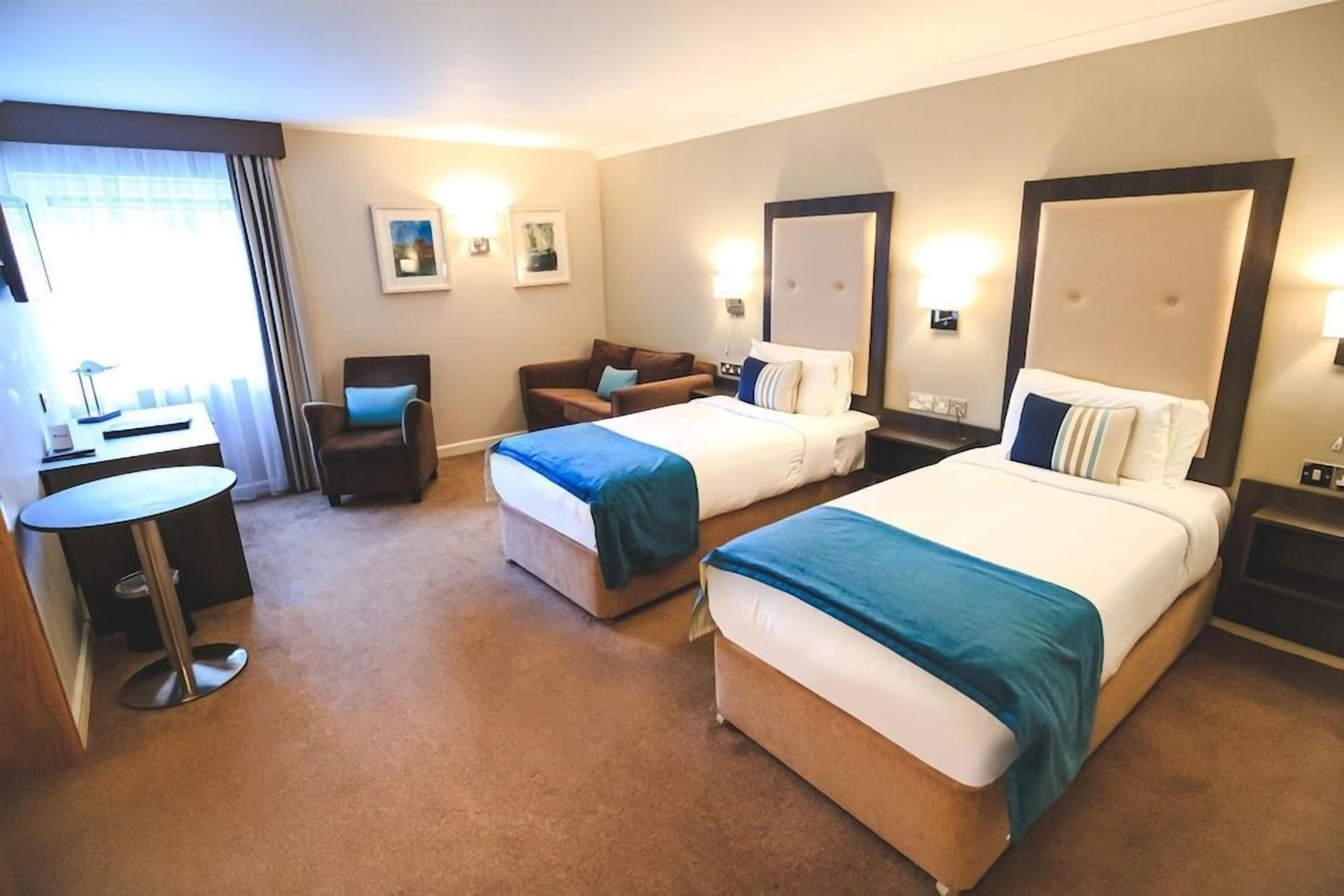 A hotel room with two beds, a desk, a chair, and a small round table.