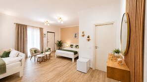 A modern hotel room with a bed, a sitting area with a table and chairs, a small white cabinet, and a large mirror. - Casa di Brenda (Frascati)