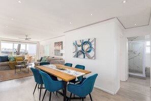 Amplia sala de estar con mesa de comedor, sillas azules, sofá y obras de arte en las paredes.
