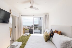 Ein Hotelzimmer mit Bett, Wandfernseher, Balkon mit Stadtblick und Deckenventilator.