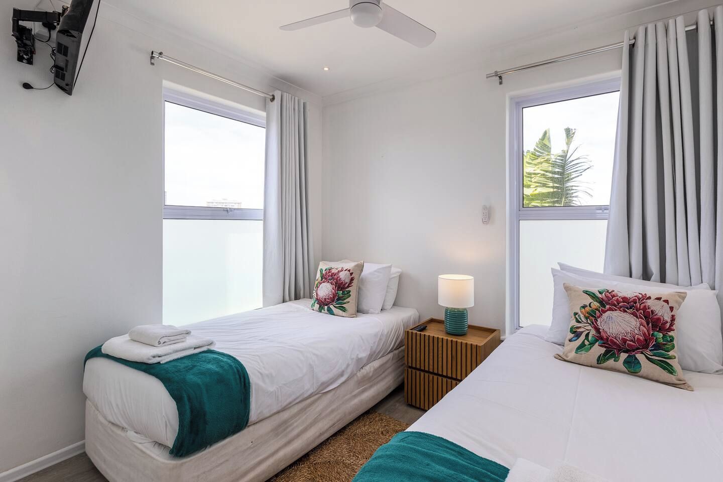 Une chambre d’hôtel avec deux lits, un ventilateur de plafond, une table de chevet avec une lampe et une fenêtre avec des rideaux.