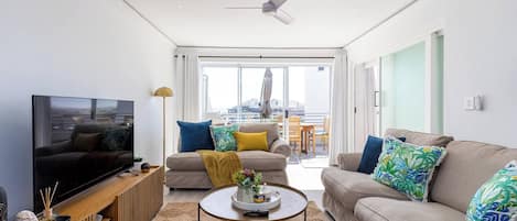 A modern living room with a flat-screen TV, two sofas, a coffee table, and a ceiling fan.