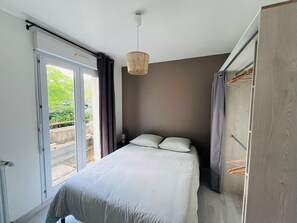 A bedroom with a bed, a hanging light fixture, a window, and a door.
