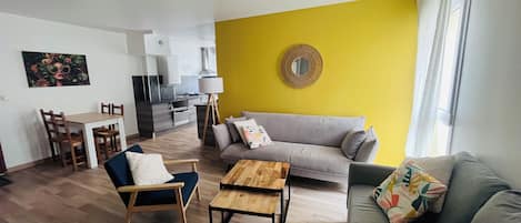 A modern living room with a sofa, a coffee table, and a dining area with chairs and a table.