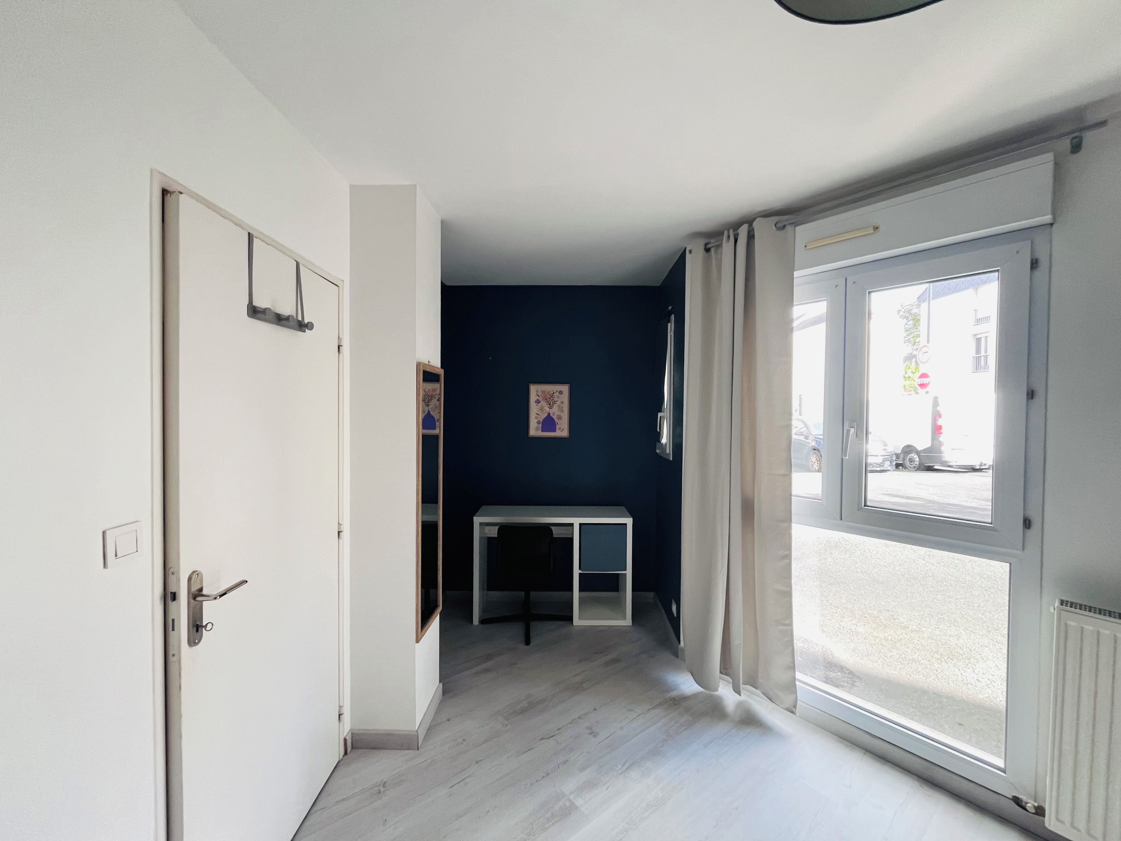 A hallway with a door on the left, a window on the right, and a small table with a chair in the center.