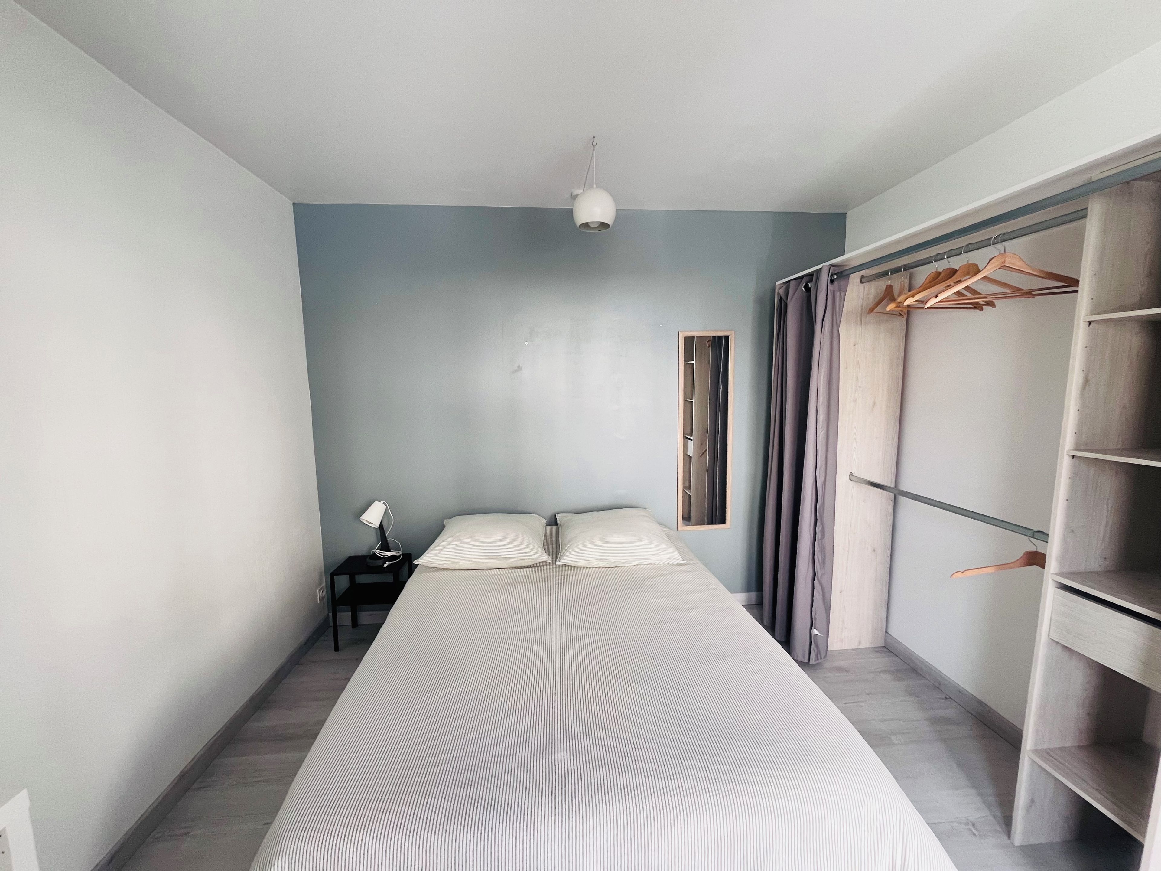 Une chambre à coucher comprenant un lit, une table de chevet, une lampe suspendue, une armoire et un miroir.