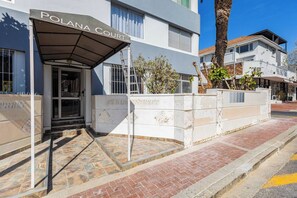 A building with a covered entrance labeled 'POLANA COURT,' a stone wall with inscriptions, and a paved sidewalk. - Kloof Street Studio Table Mountain views by ctha (Cape Town)