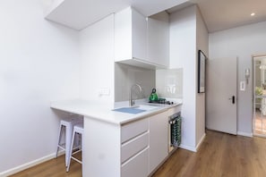 A modern kitchen with white cabinetry, a sink, a green kettle, and a small stool. - Kloof Street Studio Table Mountain views by ctha (Cape Town)