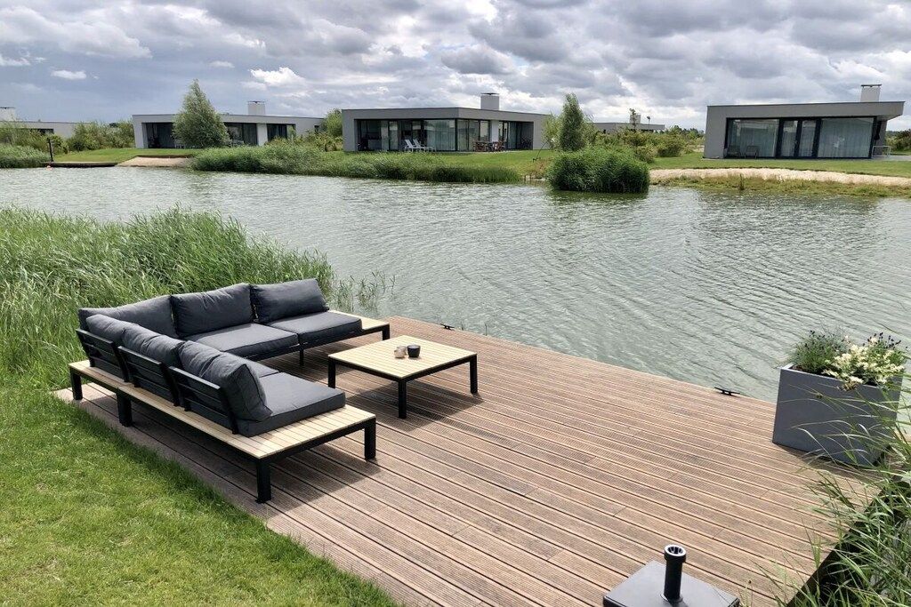 Een modern terras buiten met een bank en tafel, met uitzicht op een waterpartij en aangrenzende gebouwen.