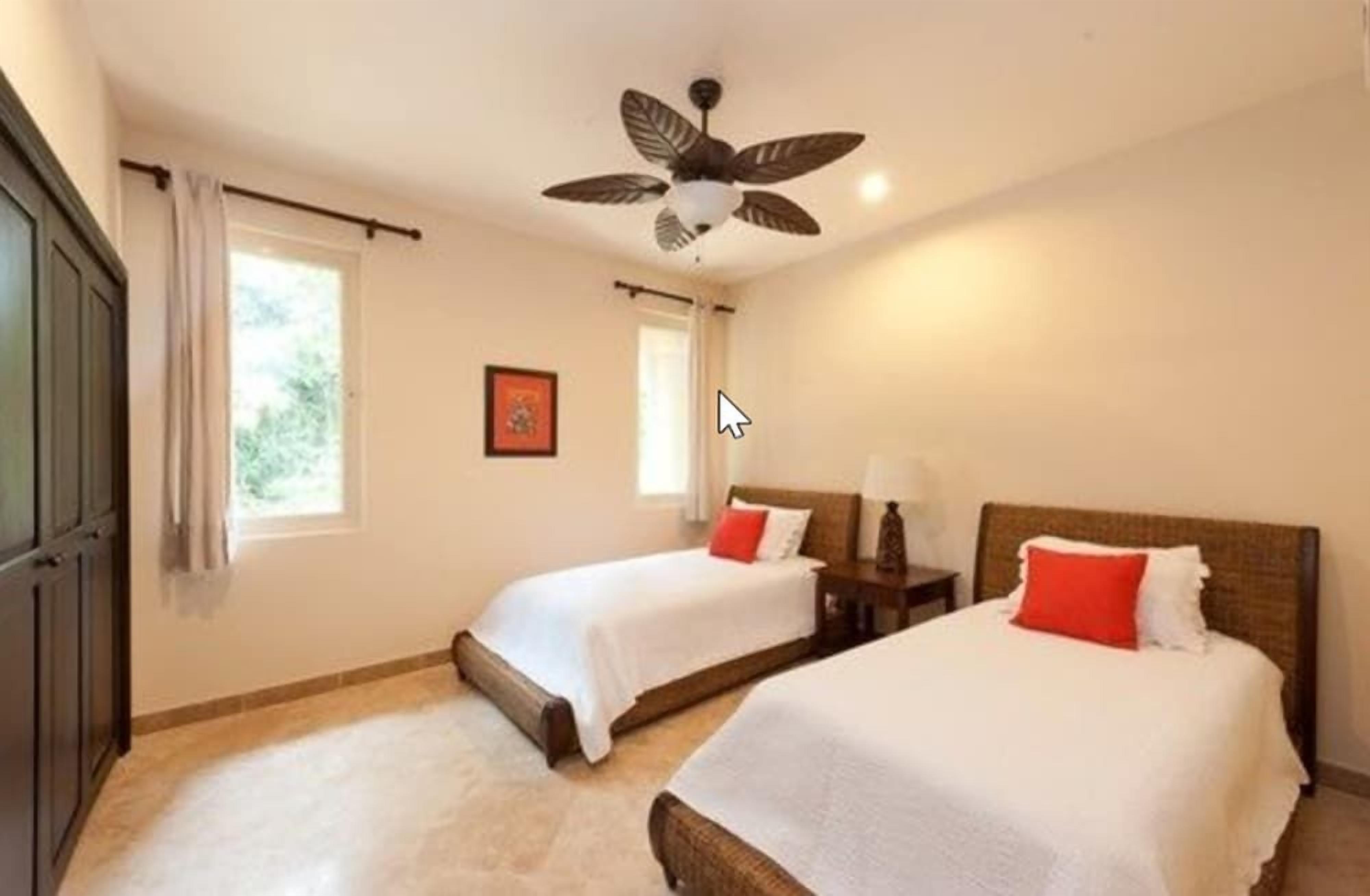 A hotel room with two beds, a ceiling fan, and a window with curtains.