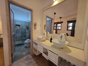 A bathroom with a large mirror, two sinks, a shower, and a toilet. - Garibaldi Inn at the Bay (Mahahual)