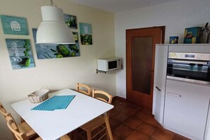 A compact kitchen with a white table, chairs, a microwave, and a refrigerator. - Holiday apartment with 2 bedrooms (Cuxhaven)