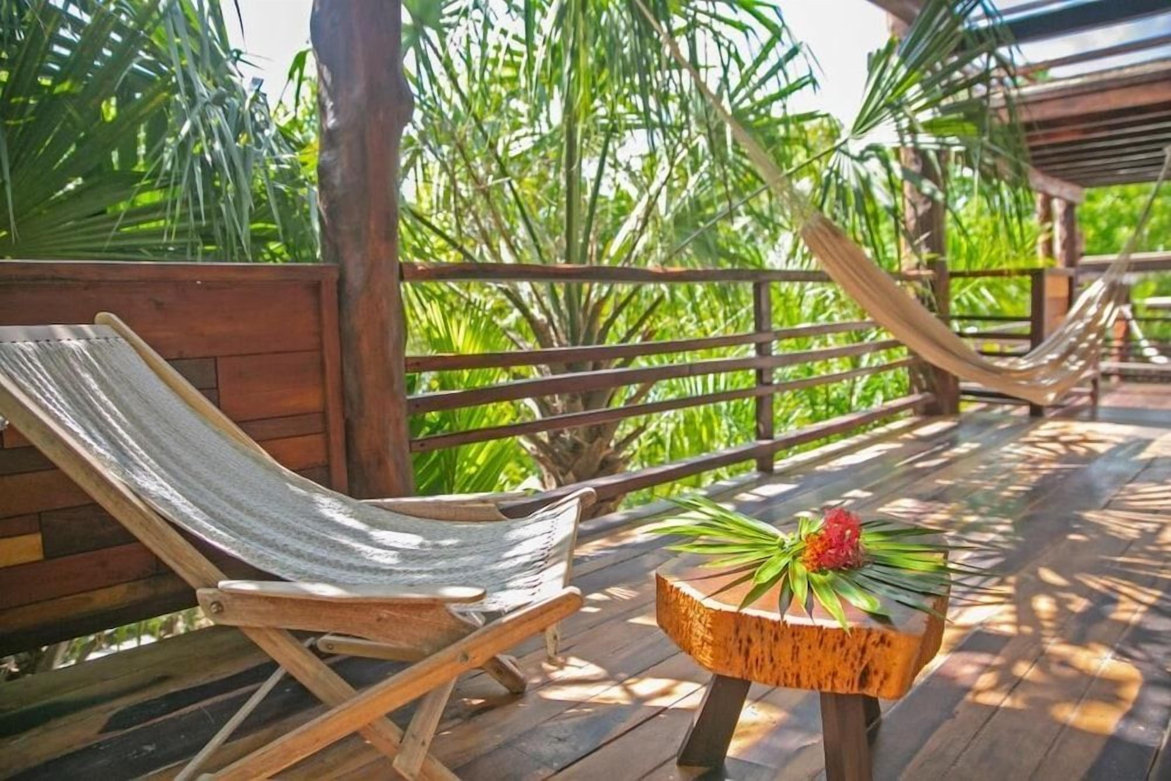 A wooden deck with a hammock chair and a small wooden table with a plant.