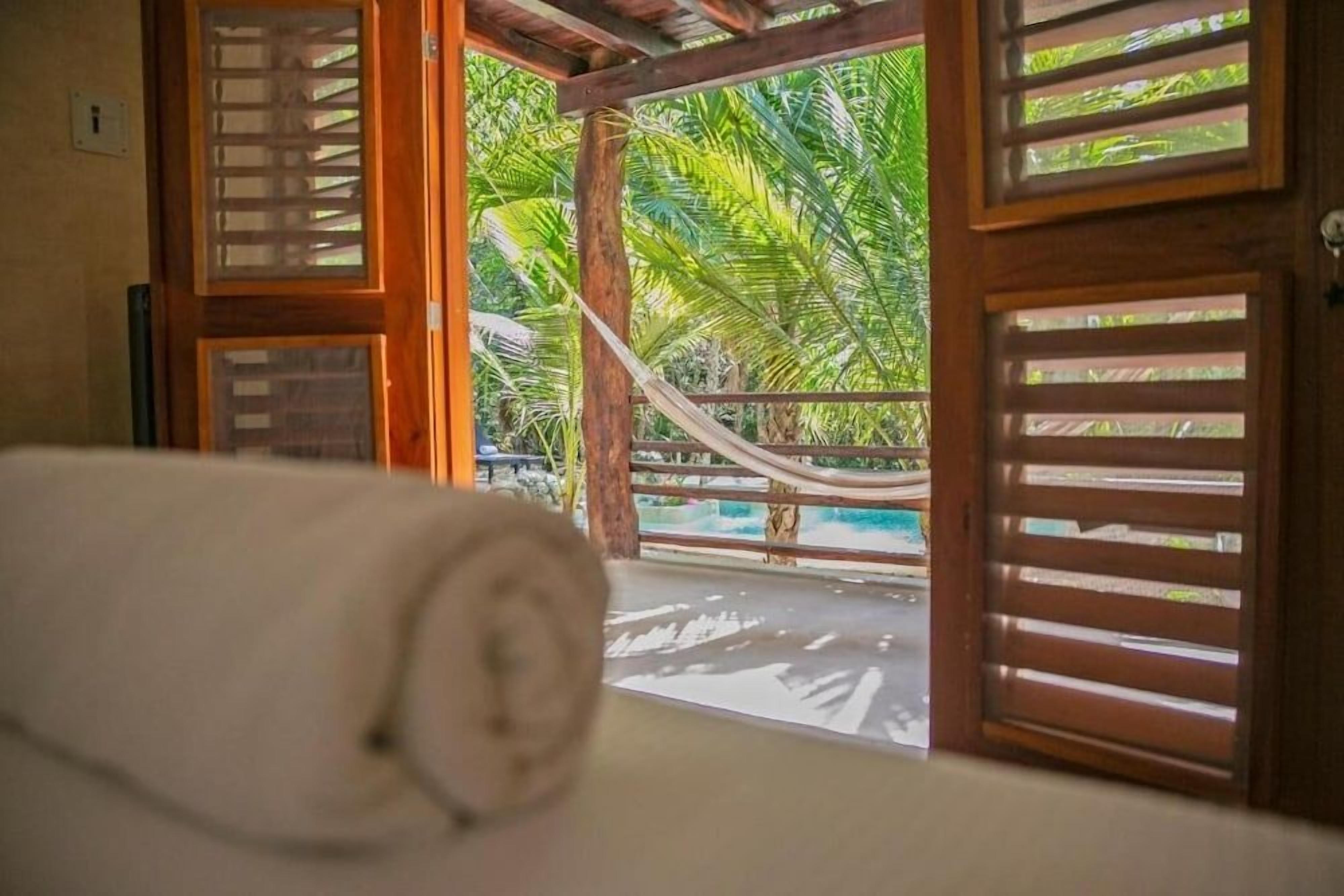 A room with a hammock, wooden slats, and a view of palm trees.