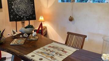 Un comedor con mesa de madera, sillas, un tapete decorativo y vistas al exterior a través de una ventana.