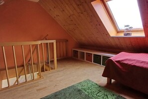 Ein Zimmer mit schrägverdeckter Decke, einem Fenster mit Aussicht, einem Bett und einer Sitzbank.